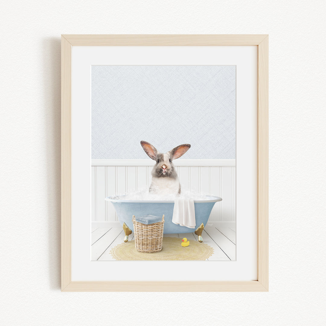 A white rabbit sitting in a blue bathtub filled with bubbles, surrounded by a yellow rubber duck and a basket of bath toys.