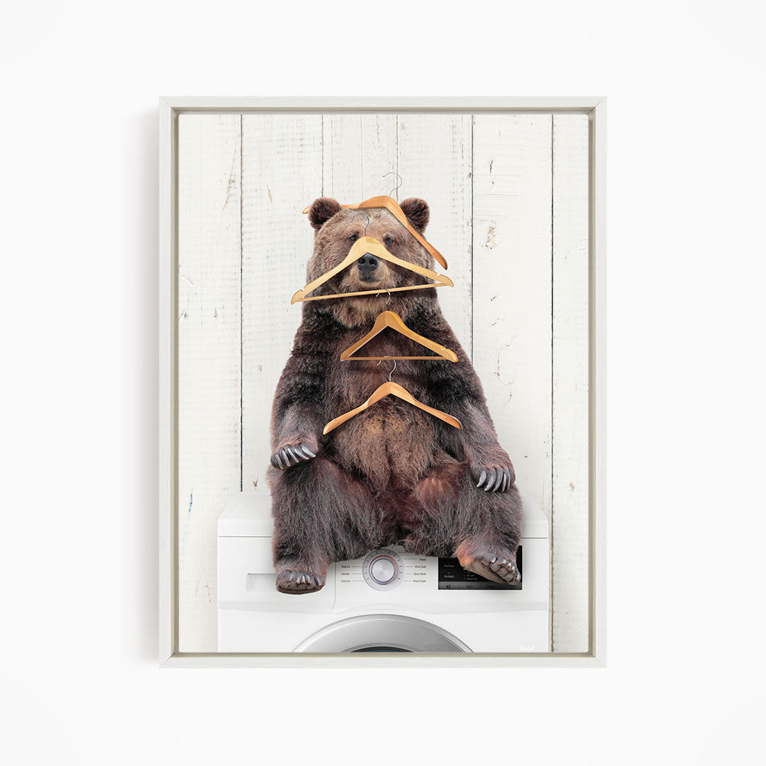 A brown bear sitting on top of a washing machine, surrounded by multiple wooden hangers.