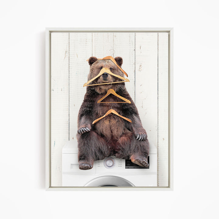 A brown bear sitting on top of a washing machine, surrounded by multiple wooden hangers.