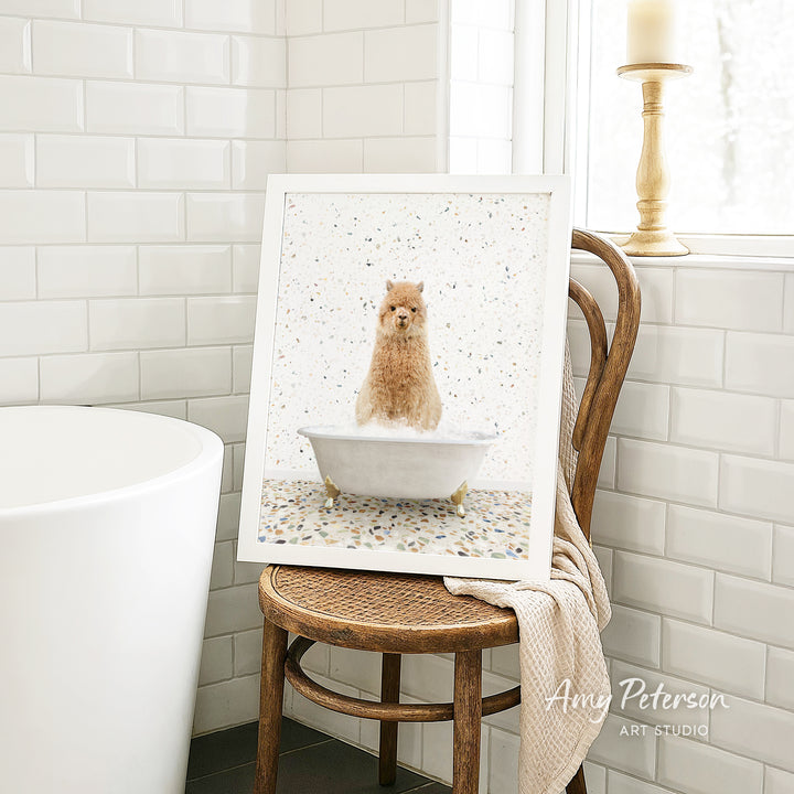 A framed image of a dog sitting in a bathtub is displayed on a wooden chair in a bathroom setting.
