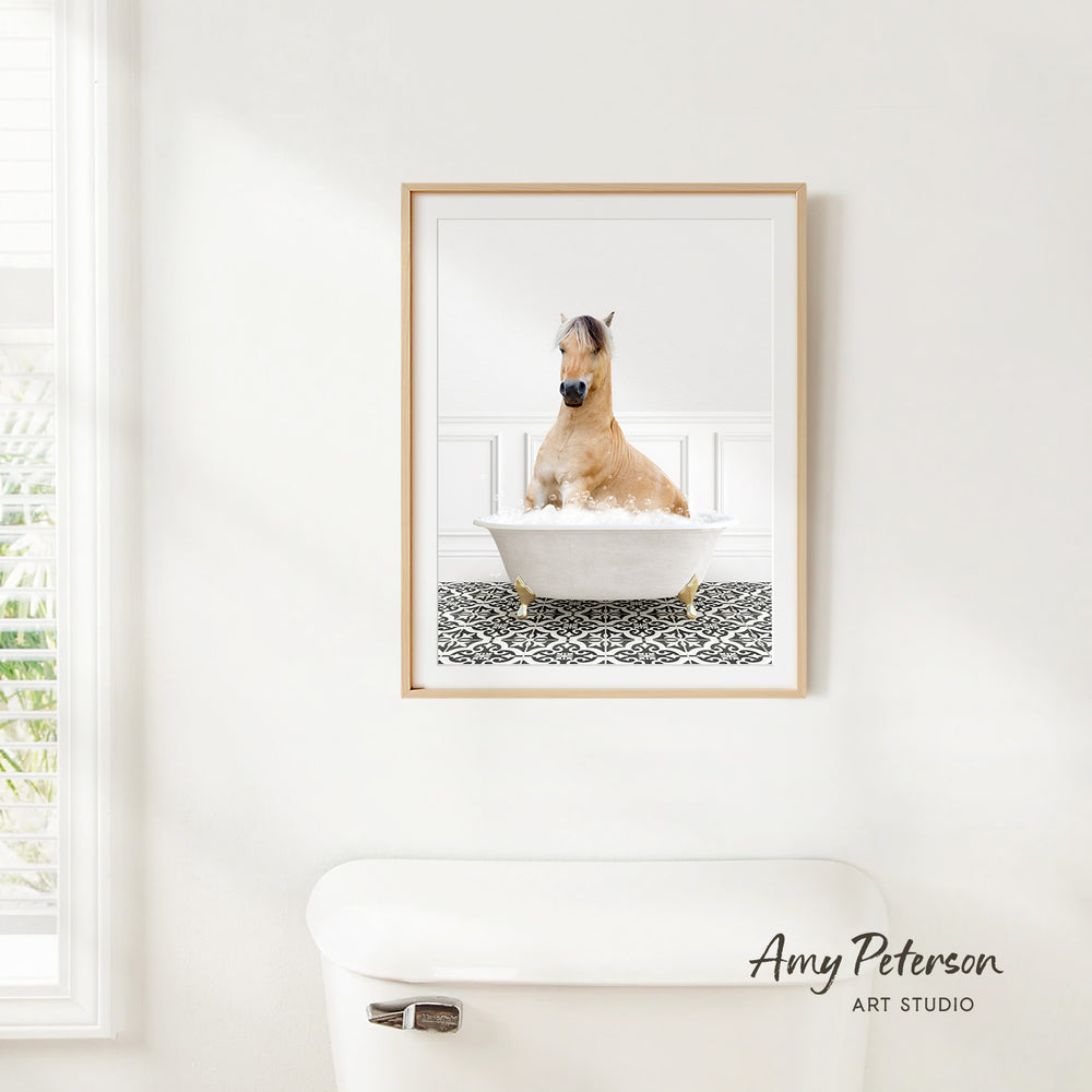 A framed image of a horse sitting in a bathtub, with a patterned tile floor beneath it.