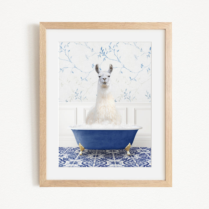 A white llama sitting in a blue bathtub filled with bubbles, with a blue and white floral patterned wall behind it.
