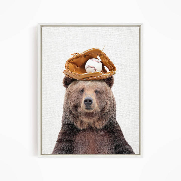 A brown bear wearing a baseball glove on its head, with a baseball resting on top of the glove.