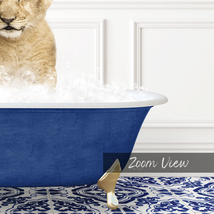 A cat is sitting in a blue bathtub filled with bubbles, with a gold claw-like object on the floor next to the tub.