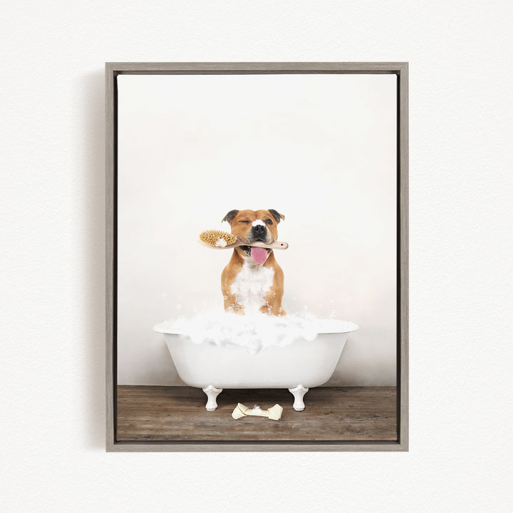 A brown and white dog sitting in a white bathtub, holding a toothbrush in its mouth, with a towel on the floor.