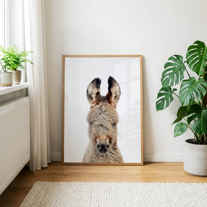 a large framed picture of a donkey's head, with a potted plant to the right and a window to the left.