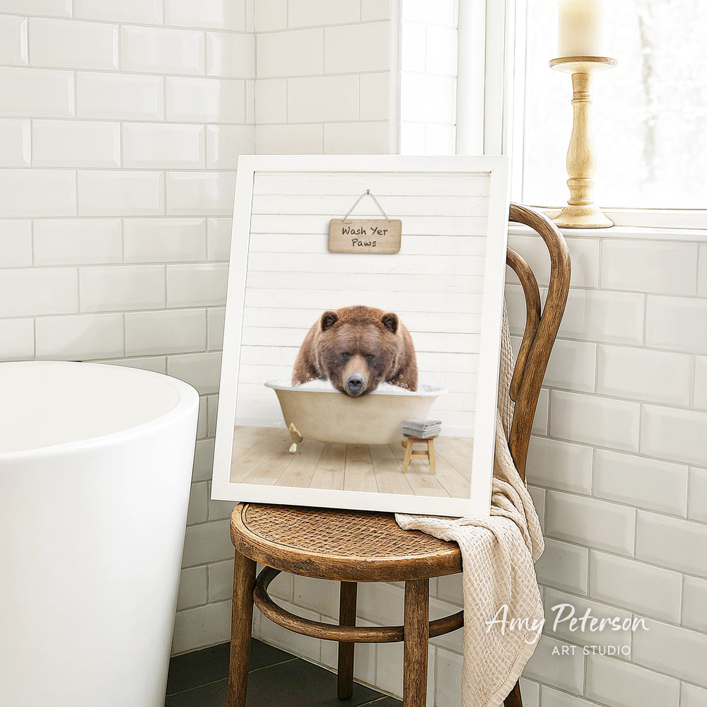 A framed image of a brown bear sitting in a bathtub, with a sign that says "Wash Your Pants" above it. The image is displayed on a wooden chair in a bathroom setting.