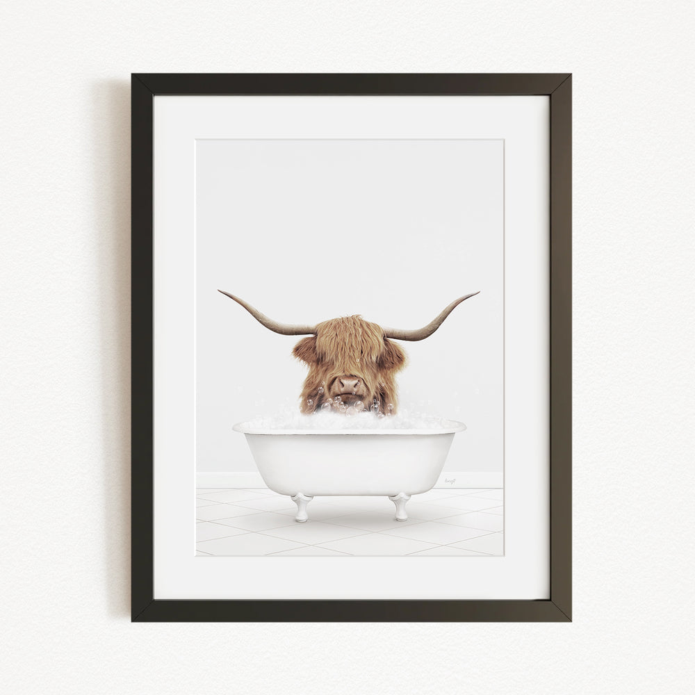 A framed image depicting a Highland cow with long horns sitting in a white bathtub filled with water.