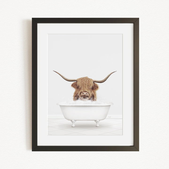 A framed image depicting a Highland cow with long horns sitting in a white bathtub filled with water.
