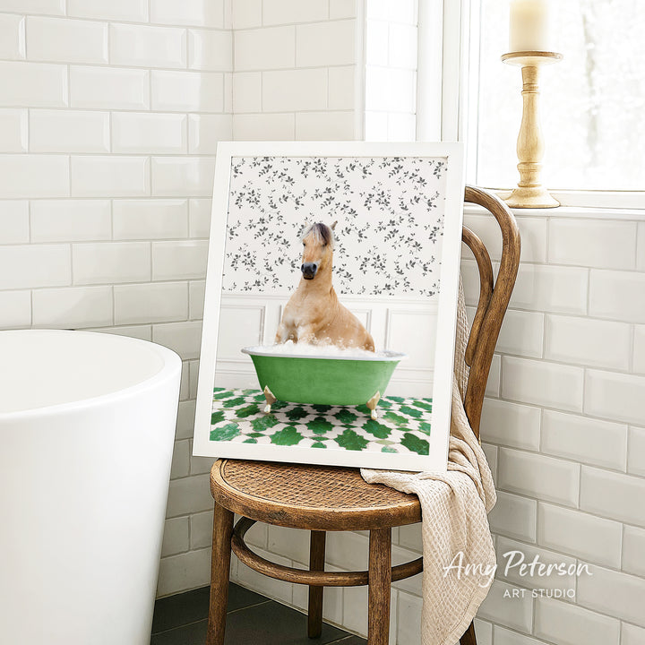 A framed image of a dog sitting in a green bathtub, surrounded by a floral pattern, is displayed on a wooden chair in a bathroom setting.