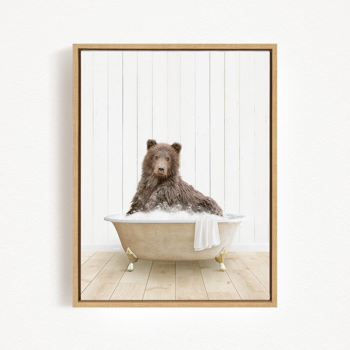 A brown bear sitting in a white bathtub filled with bubbles, with a towel hanging on the side.