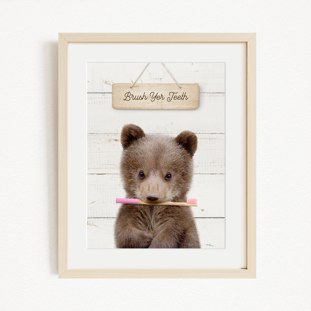 A cute brown bear holding a pink toothbrush in front of a wooden sign that says "Brush Your Teeth".