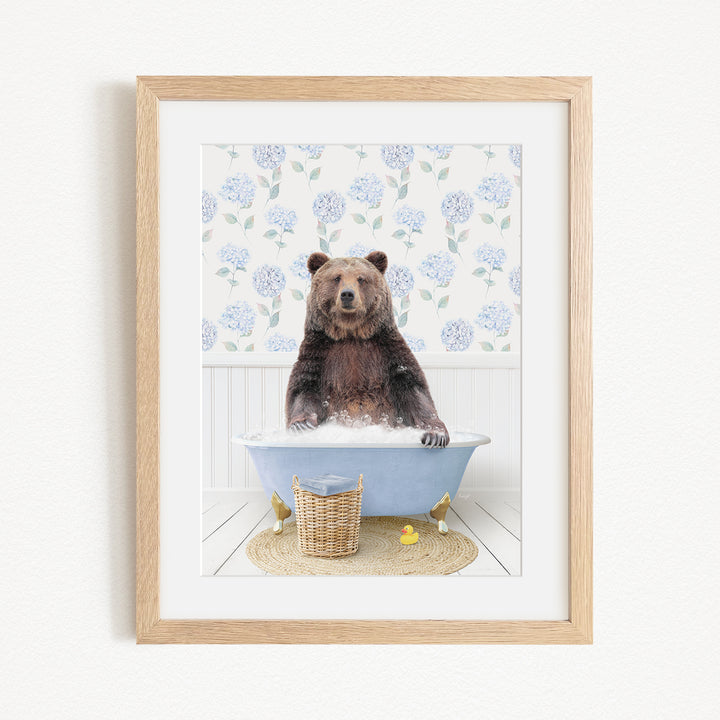 A brown bear sitting in a blue bathtub filled with bubbles, surrounded by a floral patterned wall and a basket of rubber ducks.