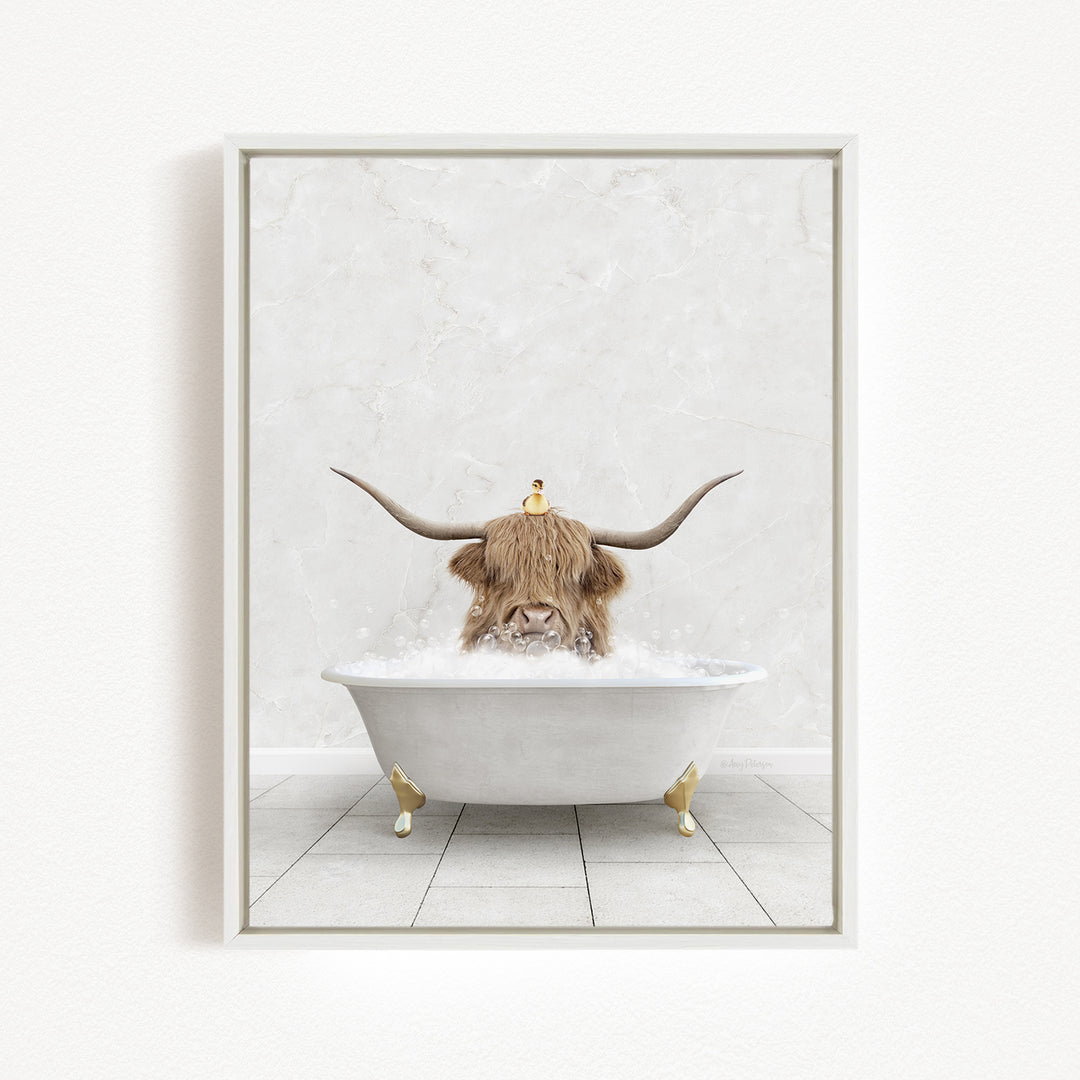 A Highland cow with large curved horns is sitting in a white bathtub filled with bubbles, with a yellow duck perched on its head.