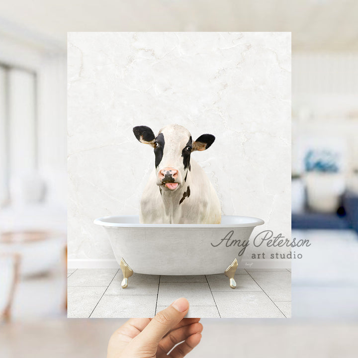 a hand holding up a photo of a cow in a bathtub