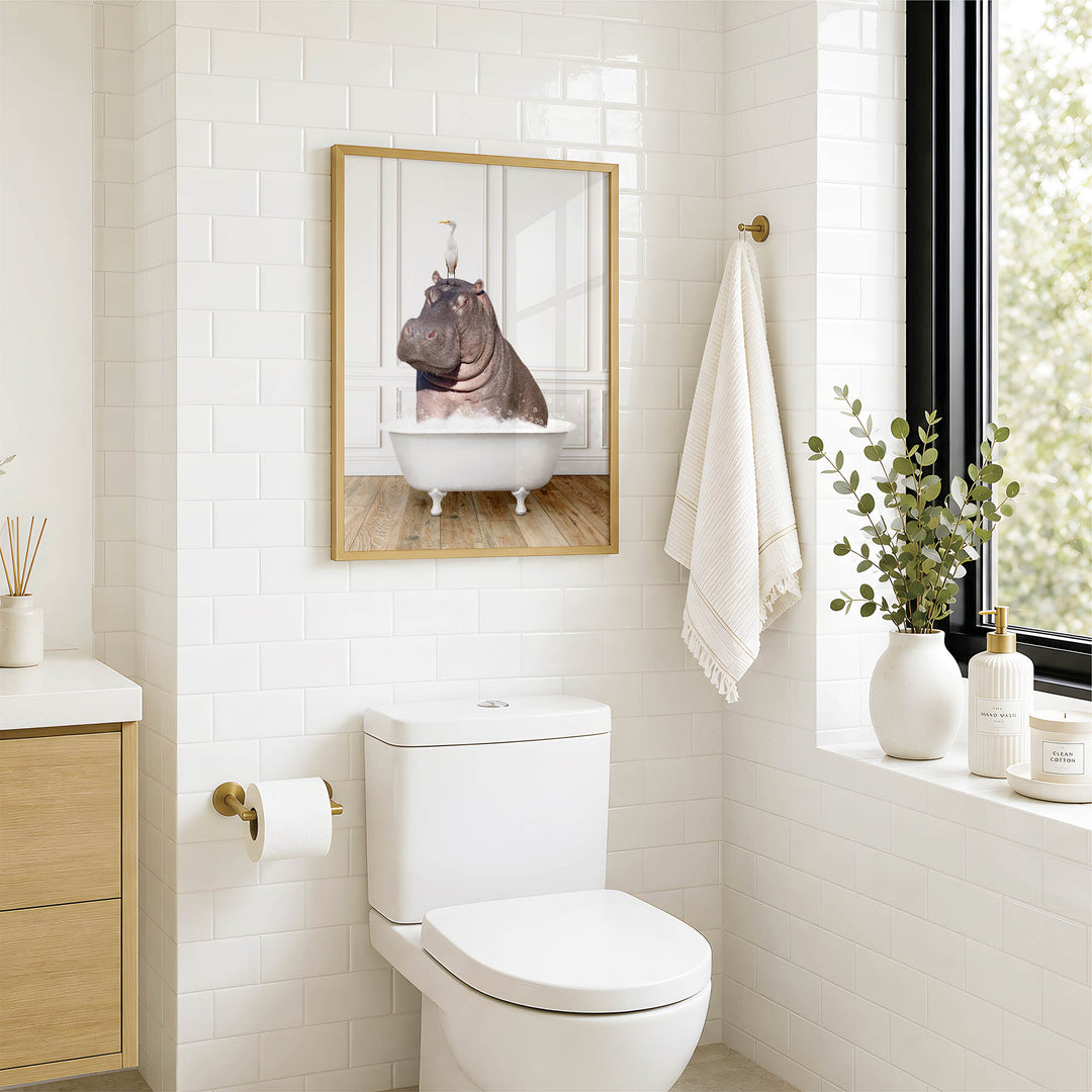 A bathroom with a white toilet, a framed image of a hippopotamus in a bathtub, and a window with greenery outside.