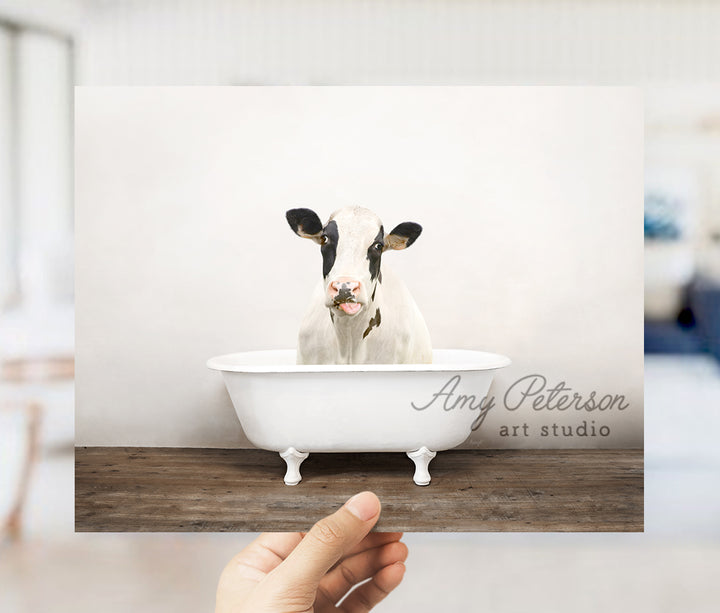 a hand holding a photo of a cow in a bathtub