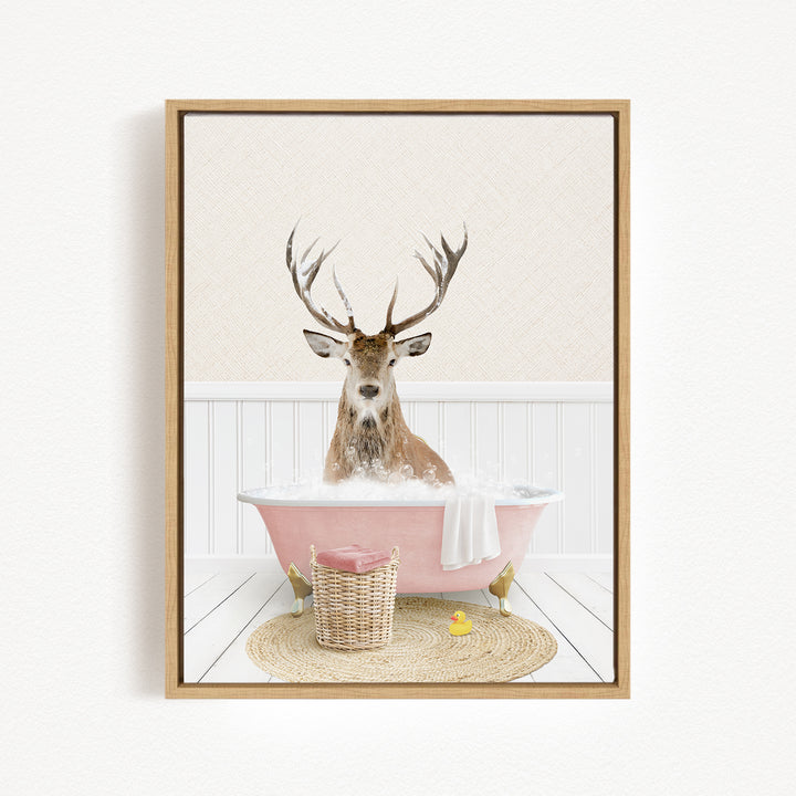 A deer with antlers is sitting in a pink bathtub filled with bubbles, surrounded by a basket of bath toys and a yellow rubber duck.