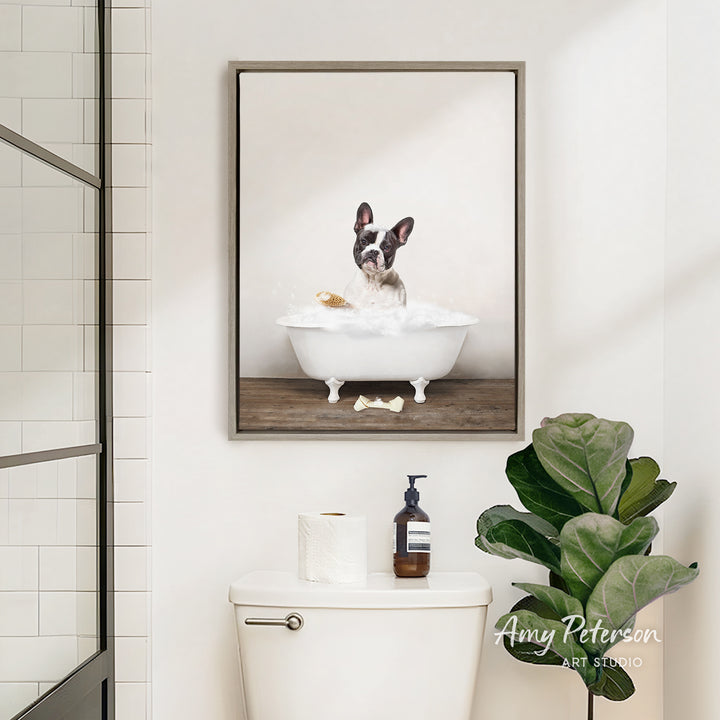 A framed image of a dog sitting in a bathtub, surrounded by bubbles, is displayed on the wall above a white toilet in a bathroom.