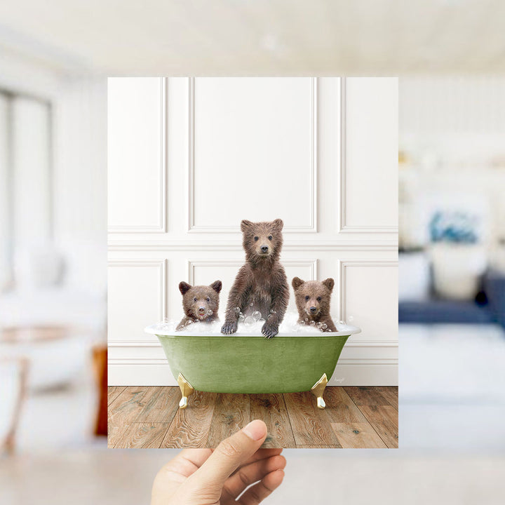 A hand holds up a framed image of three adorable brown bears sitting in a green bathtub, with one bear sitting in the center and the other two on either side.