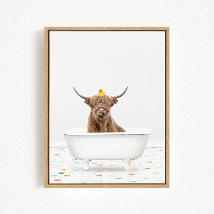 A brown cow with long horns is sitting in a white bathtub, with a rubber duck perched on its head.