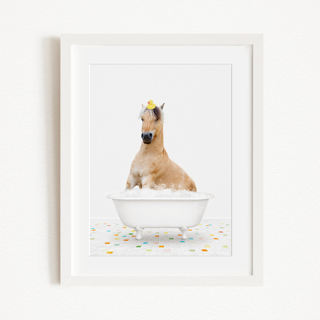 A light brown horse is sitting in a white bathtub filled with bubbles, wearing a yellow rubber duck on its head.