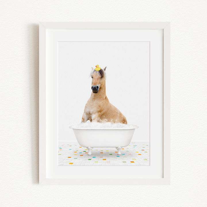 A light brown horse is sitting in a white bathtub filled with bubbles, wearing a yellow rubber duck on its head.