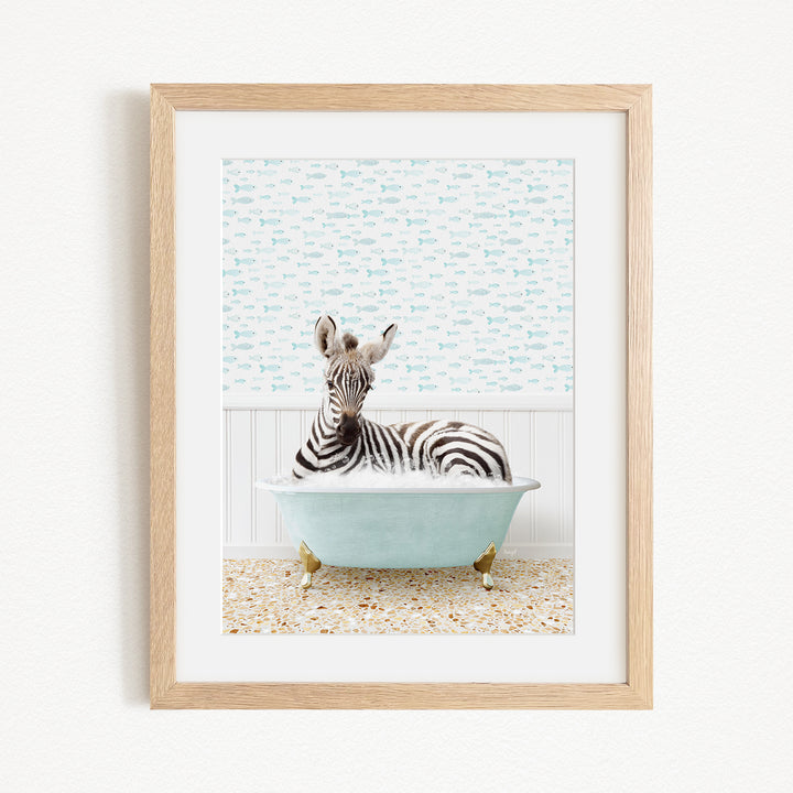 A zebra is sitting in a light blue bathtub, surrounded by a patterned tile floor and a white wall with a blue and white fish wallpaper.