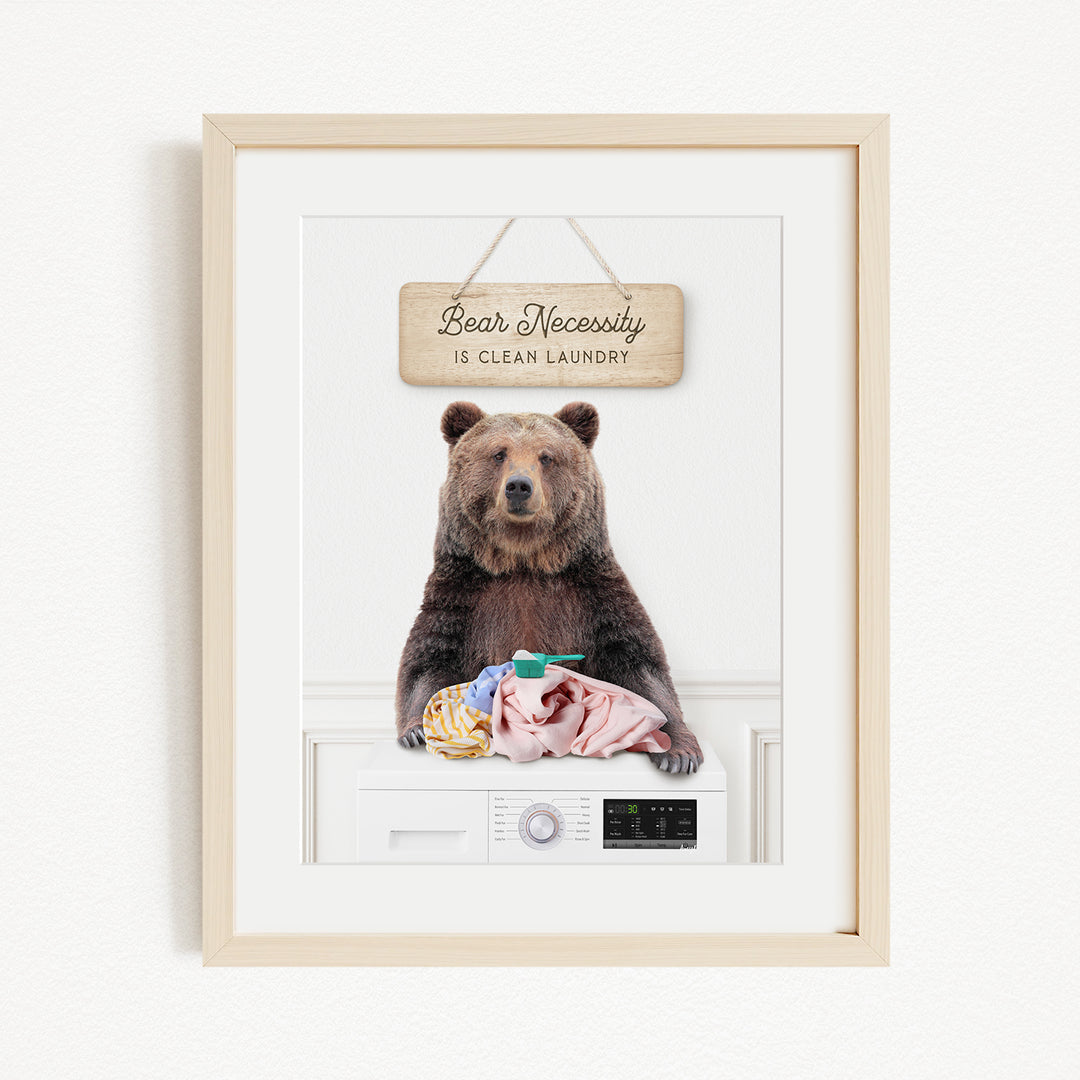 A framed image of a brown bear sitting on a washing machine, with a sign above that says "Bear Necessity is clean laundry".