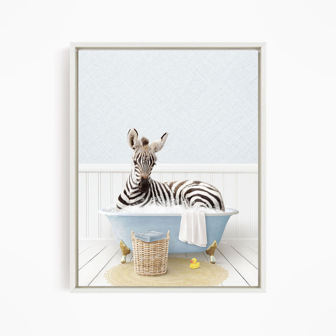 A zebra is sitting in a blue bathtub, surrounded by a yellow rubber duck and a wicker basket.