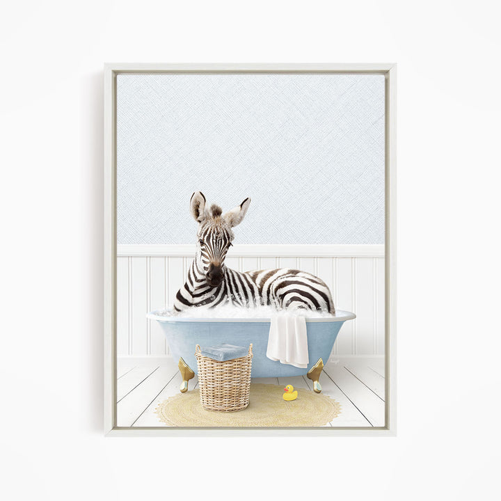 A zebra is sitting in a blue bathtub, surrounded by a yellow rubber duck and a wicker basket.