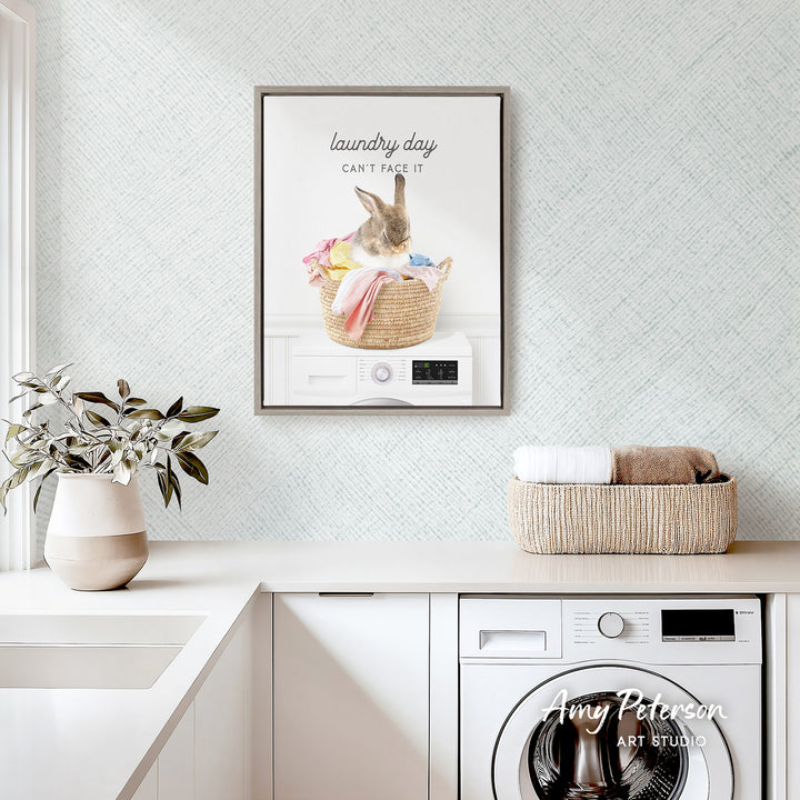 a laundry room with a framed poster of a rabbit sitting in a basket of laundry, a white washing machine, and a basket of folded towels on the counter.