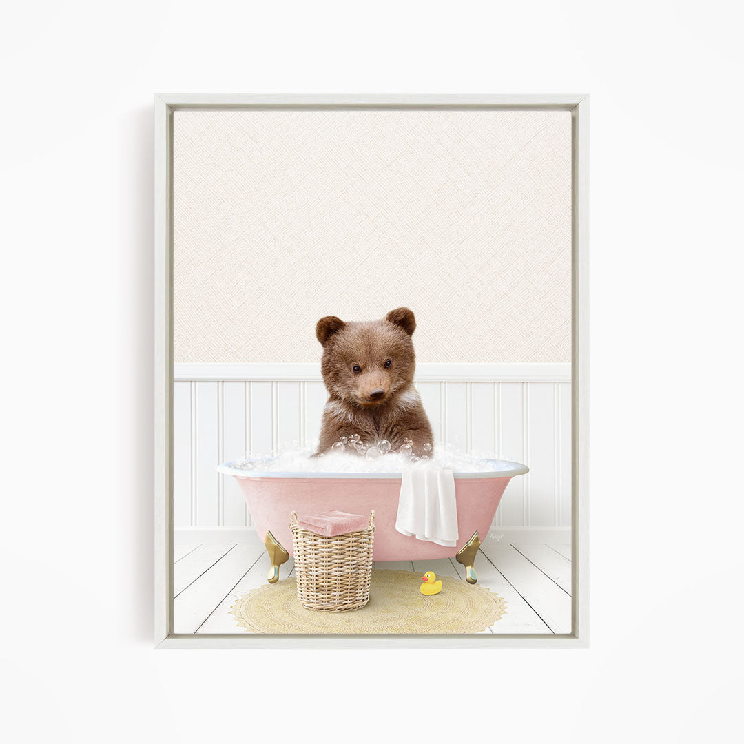 A brown bear sitting in a pink bathtub filled with bubbles, surrounded by a yellow rubber duck and a basket.