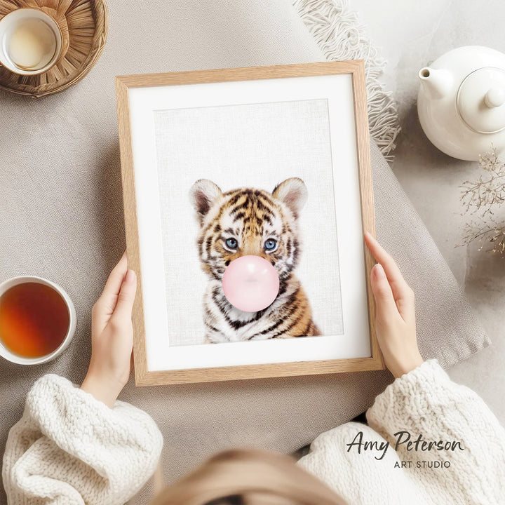 A person is holding a framed picture of a tiger blowing a bubble with a pink bubble gum bubble.