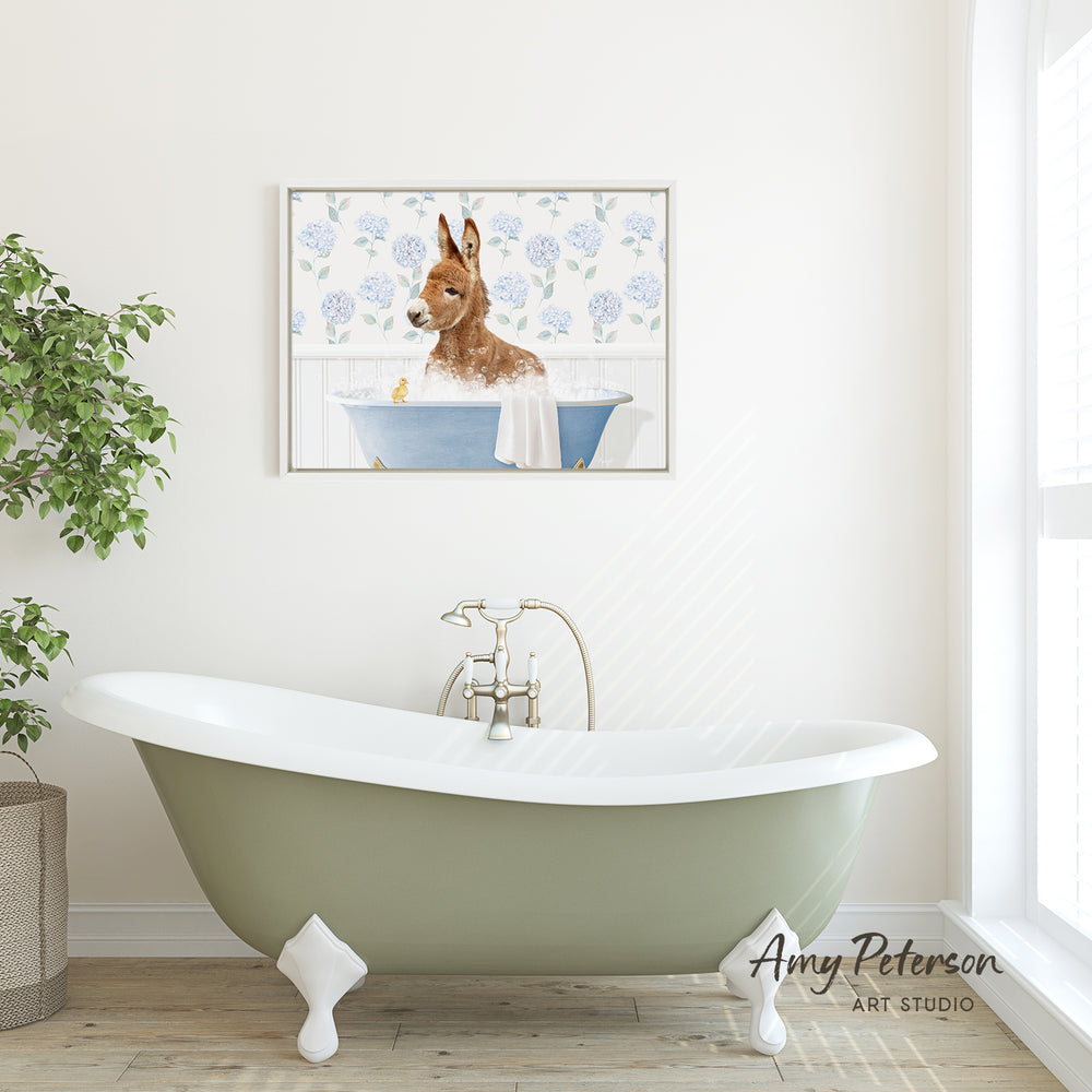 A green clawfoot bathtub with a white towel hanging over the side, set against a white wall with a framed picture of a rabbit in a bathtub.