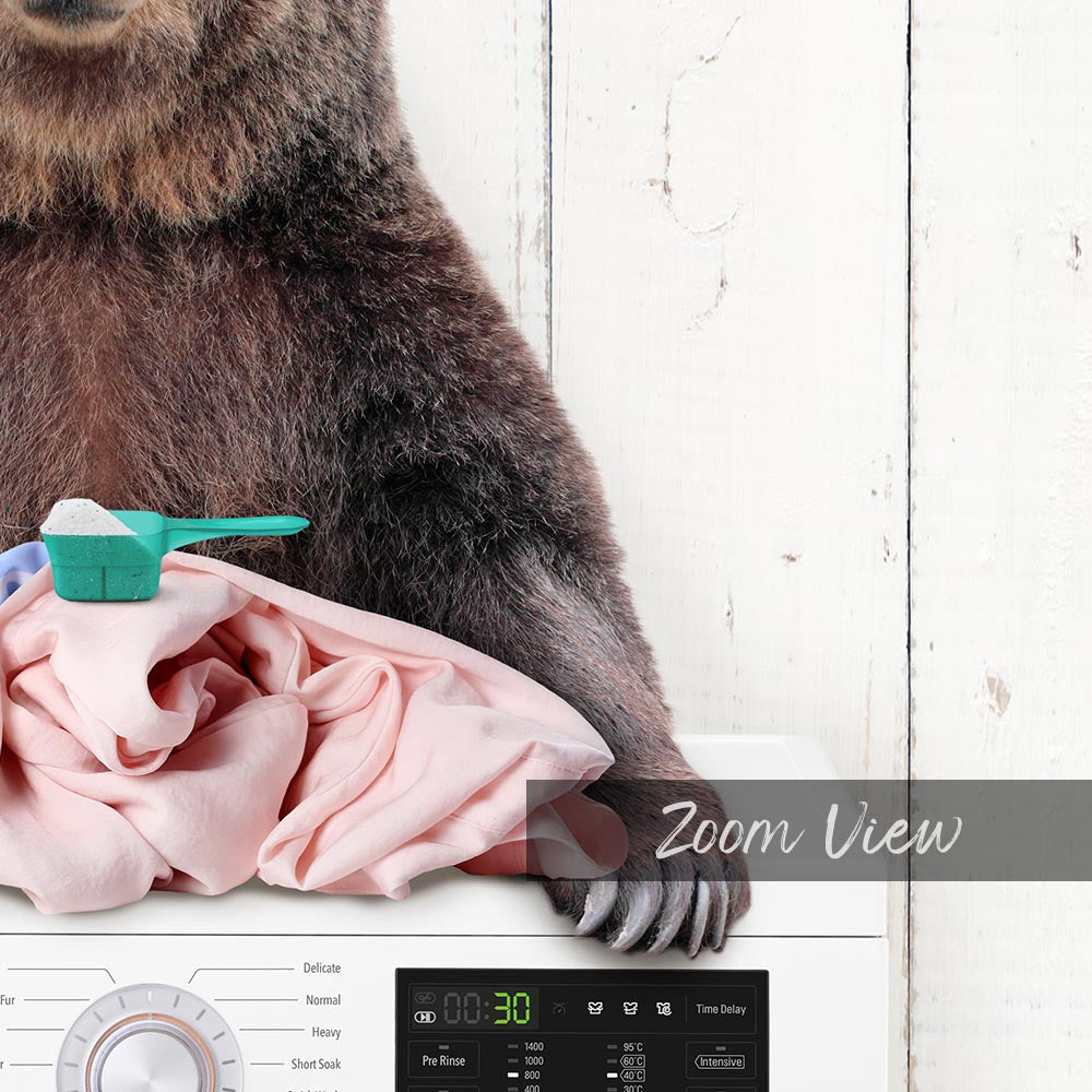 A bear is sitting on top of a washing machine, with a pink fabric next to it.