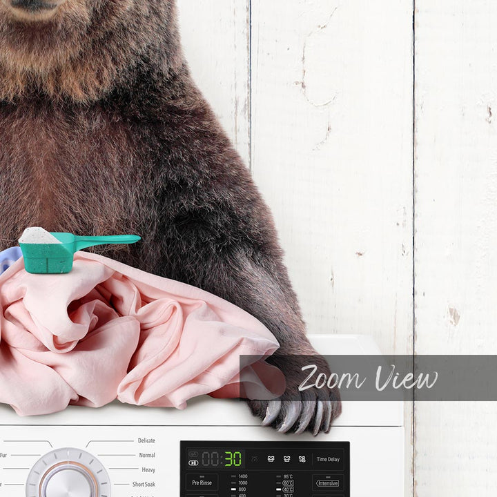 A bear is sitting on top of a washing machine, with a pink fabric next to it.