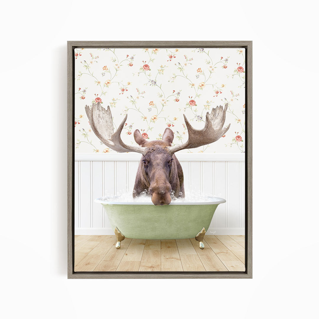 A moose with large antlers is sitting in a green bathtub, surrounded by a floral wallpaper.