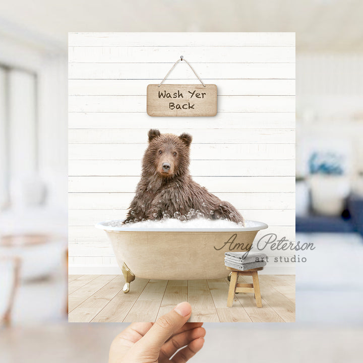 a hand holding a photo of a bear in a bathtub