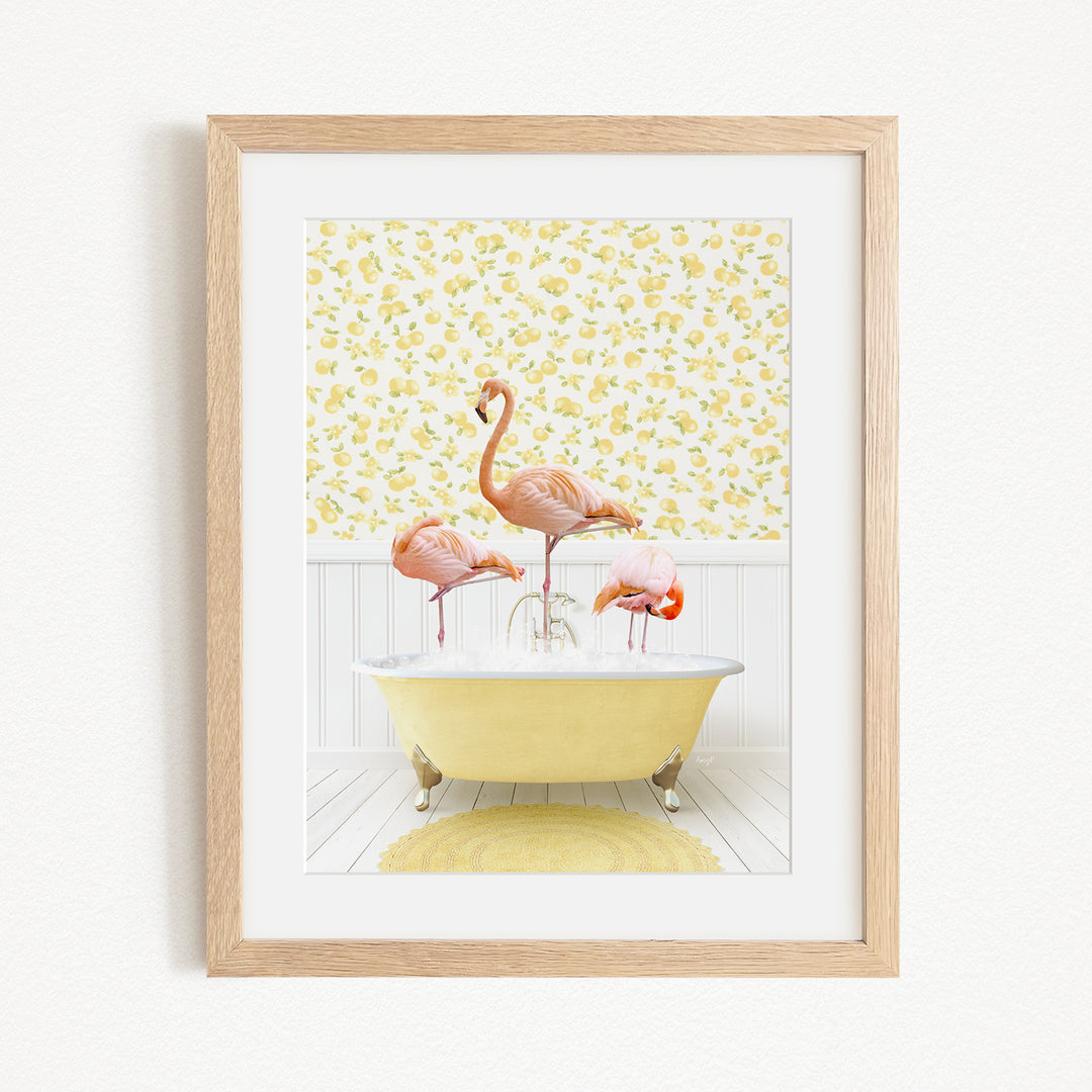 A framed image depicting three pink flamingos standing in a yellow bathtub, with a yellow floral wallpaper in the background.