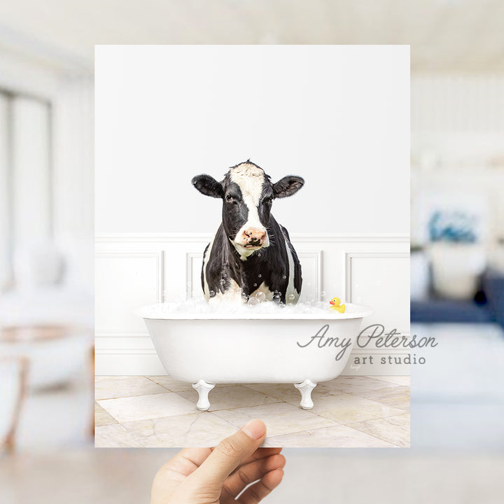 a hand holding up a photo of a cow in a bathtub