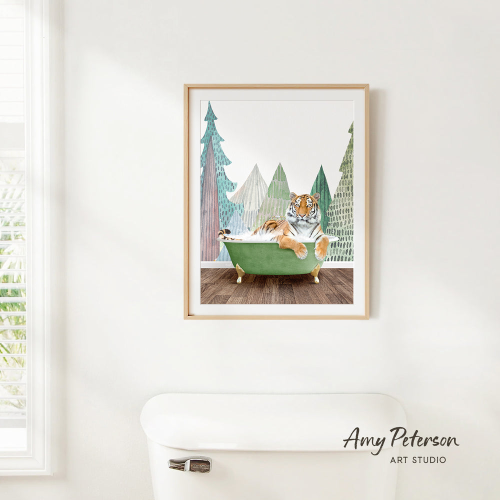 A framed print of a tiger sitting in a green bathtub, surrounded by trees and a snowy landscape, hangs on a white wall.