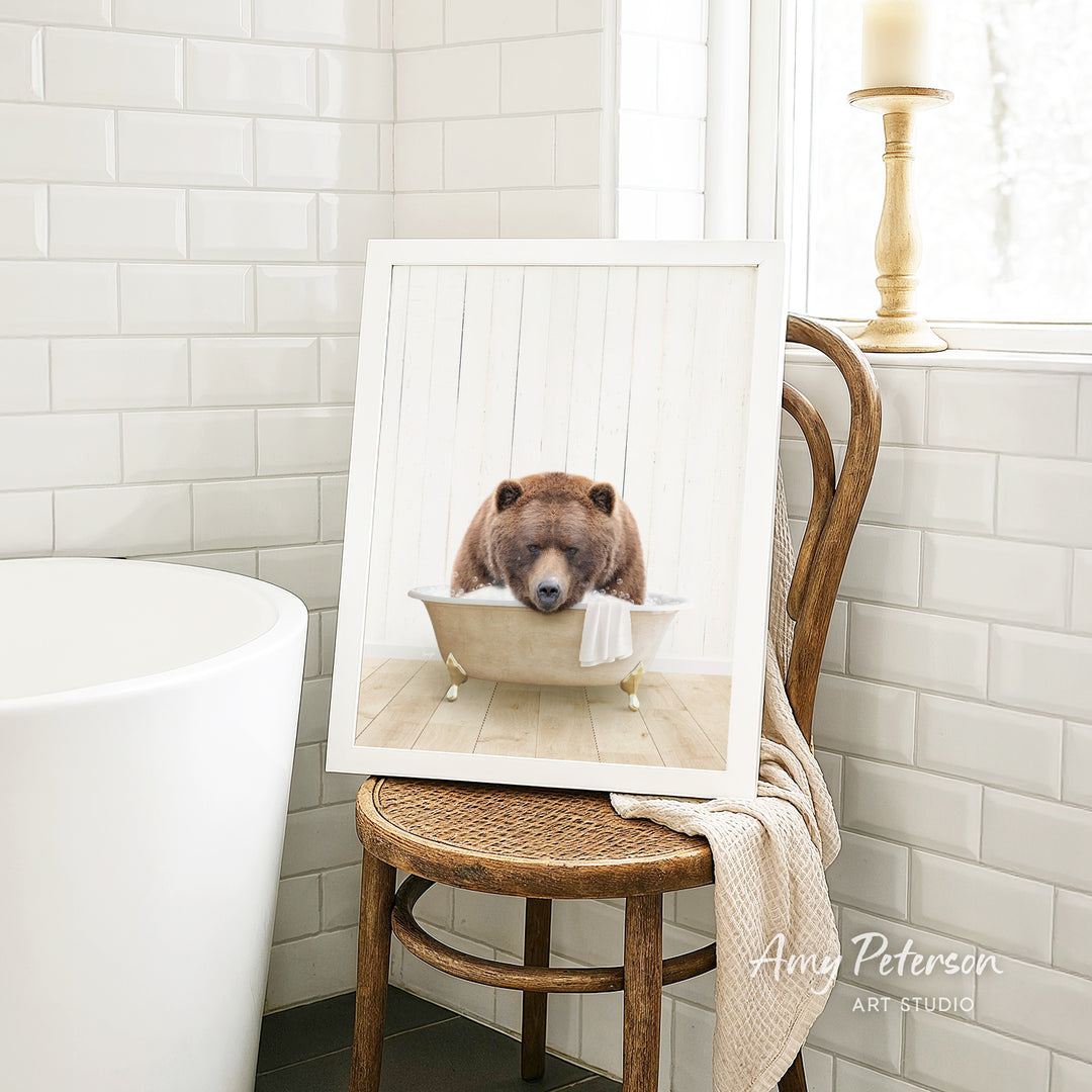 A framed image of a brown bear sitting in a bathtub, with a towel draped over the side of the tub.