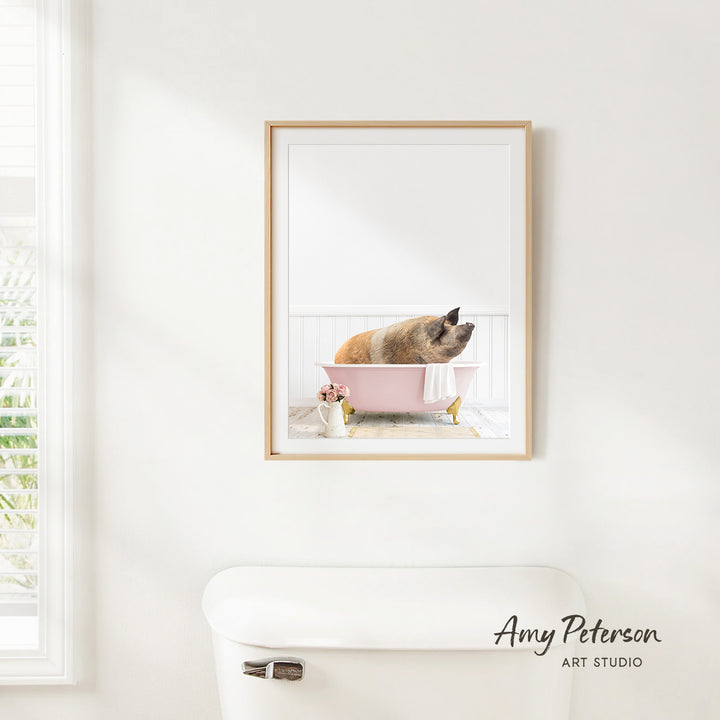 A framed image of a pig sitting in a pink bathtub, with a window and a white toilet visible in the background.