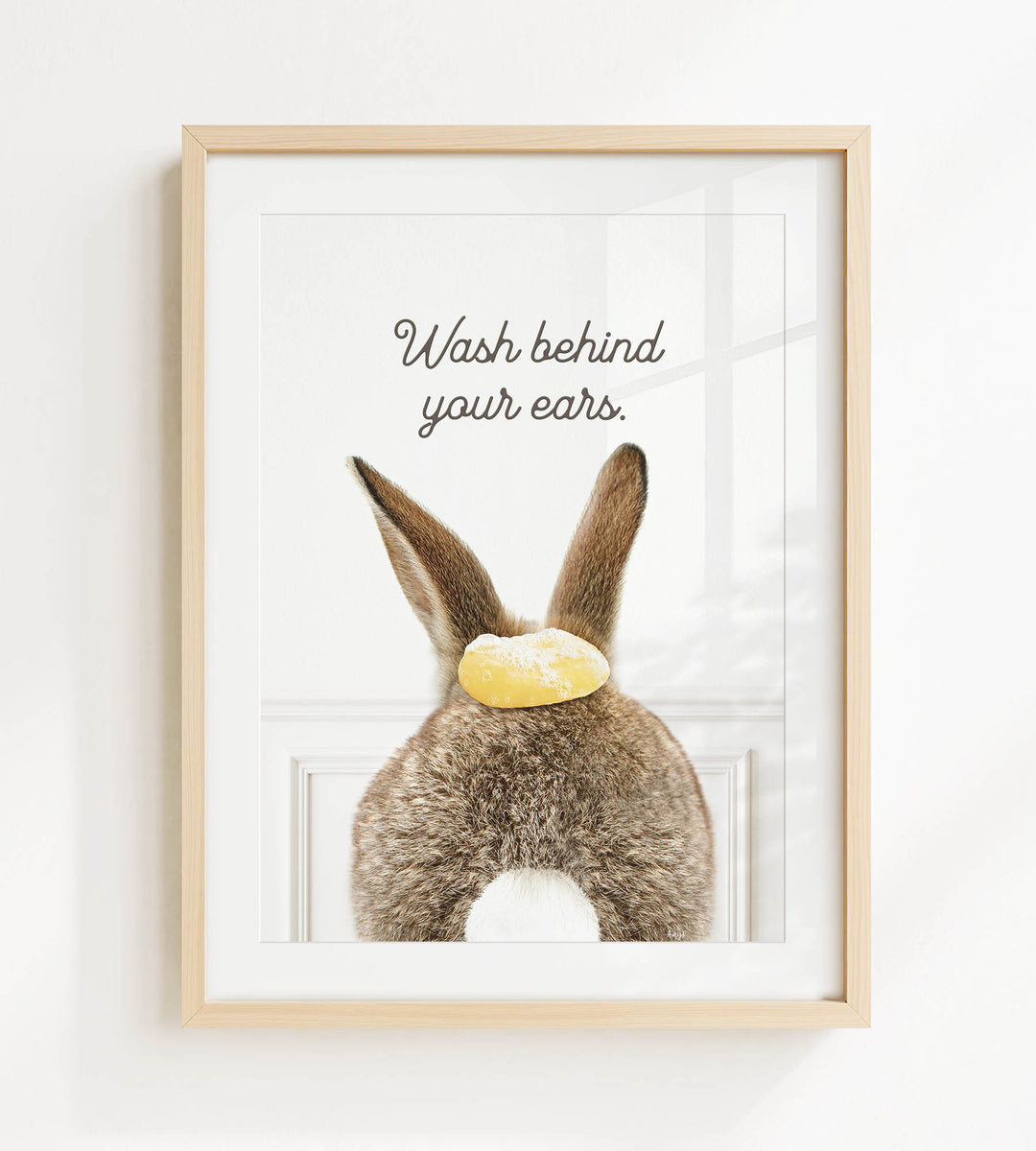 A framed image of a rabbit with a yellow object on its head, accompanied by the text "Wash behind your ears."