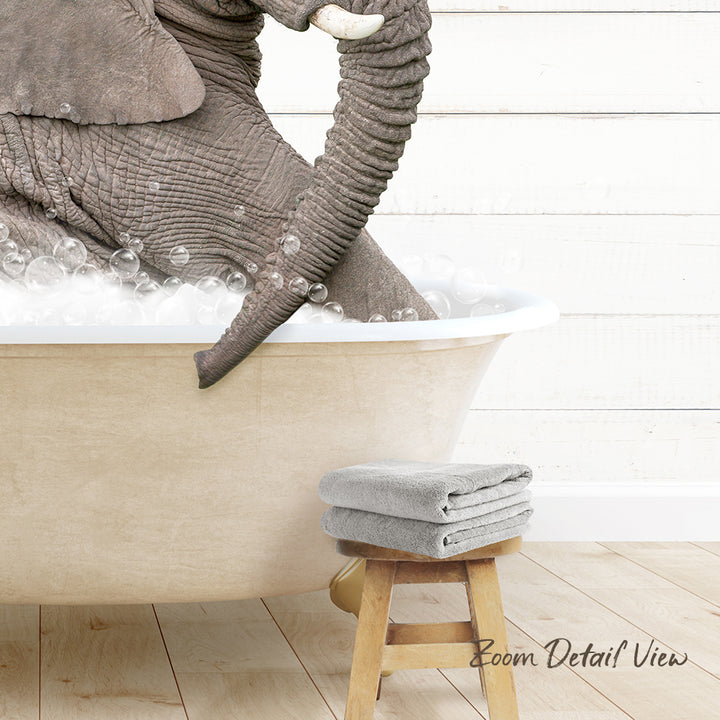 A large elephant is taking a bath in a white bathtub, surrounded by bubbles, with a wooden stool nearby.