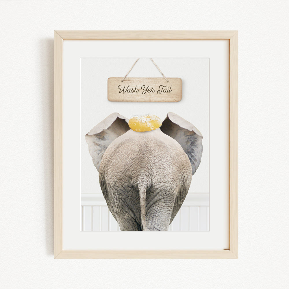 A framed image of an elephant with a sign above it that says "Wash Your Tail".