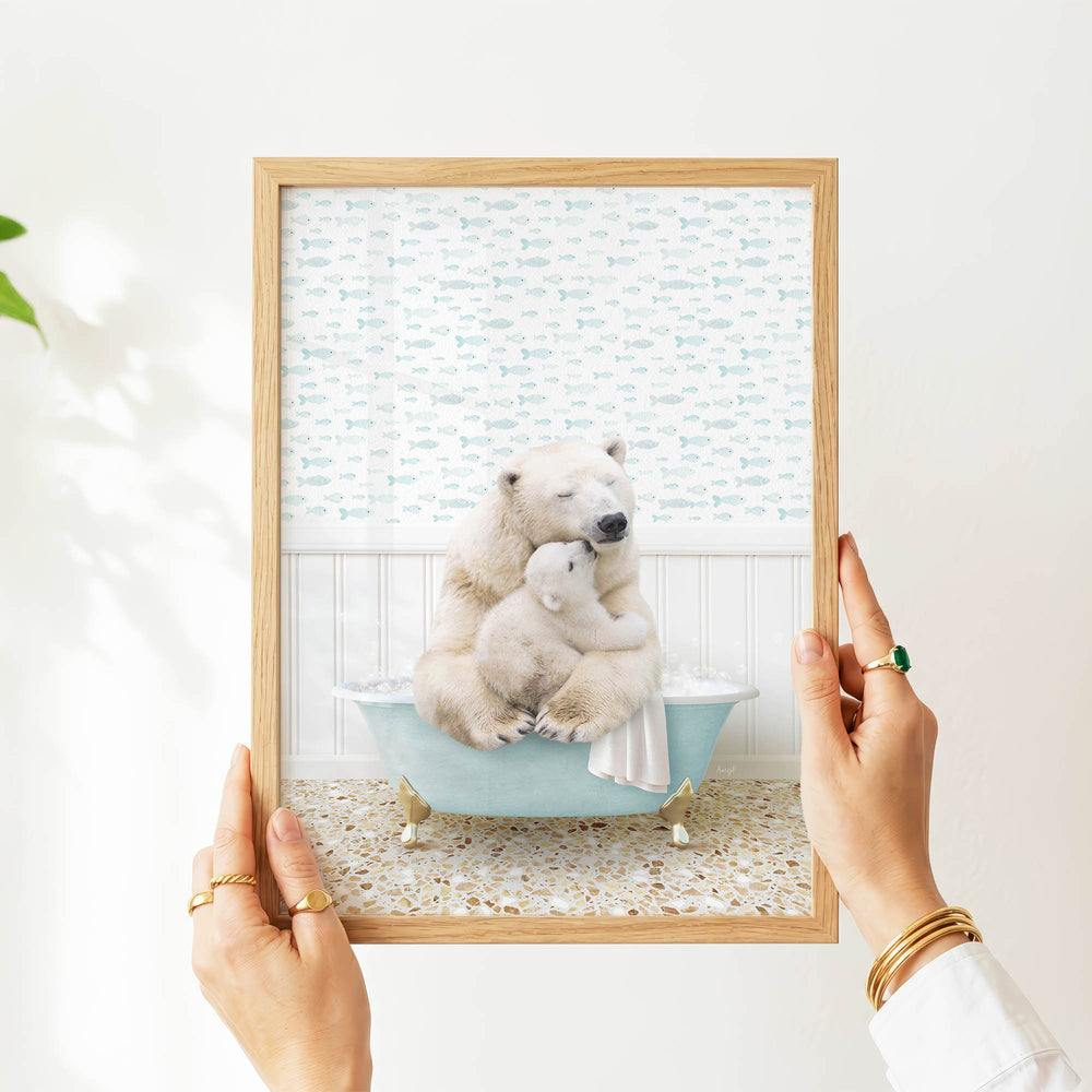 A person's hands are holding a framed image of a polar bear sitting in a bathtub, with a baby polar bear resting on its lap.
