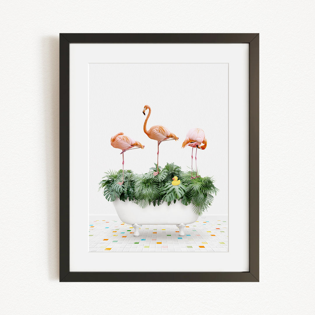 A framed image depicting three flamingos standing in a white bathtub filled with green plants and flowers, set against a white background.