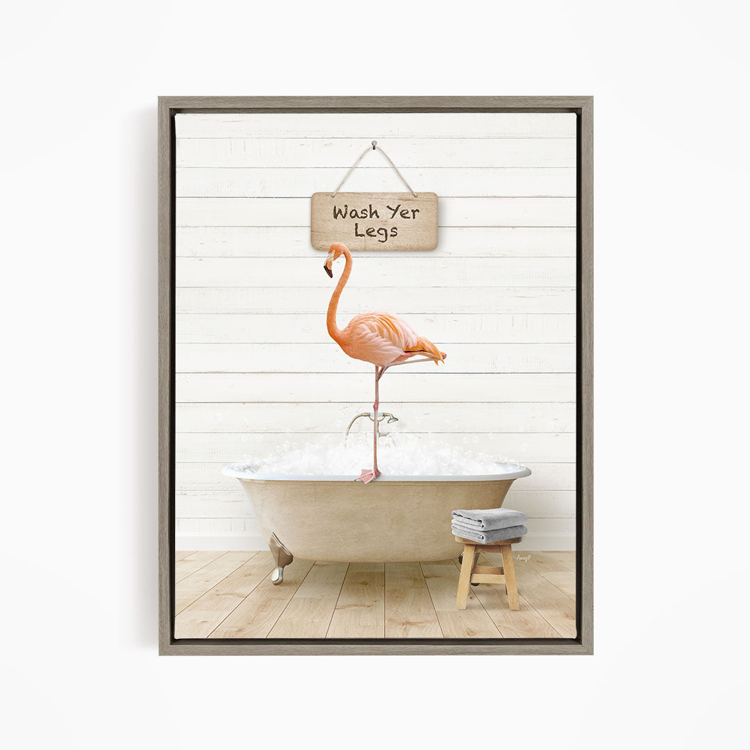 A framed image depicting a pink flamingo standing in a bathtub, with a sign above it that says "Wash Your Legs".